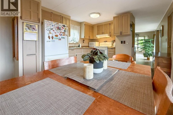 Kitchen and dining area with tan cabinets, wooden furniture, and a view of the living room with plants. - 2129 Rama Rd, Campbell River
