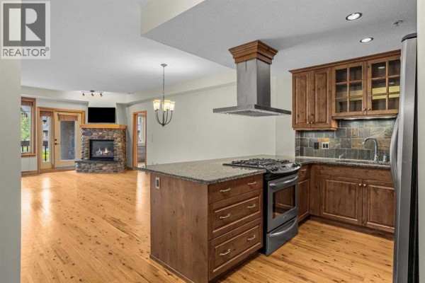Open-concept living area and kitchen with a fireplace and island. - 213, 505 Spring Creek Drive, Canmore