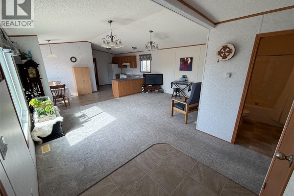An open-concept living room and kitchen area in a mobile home with beige walls and grey carpet. - 213 - 217 2nd Street W, Climax