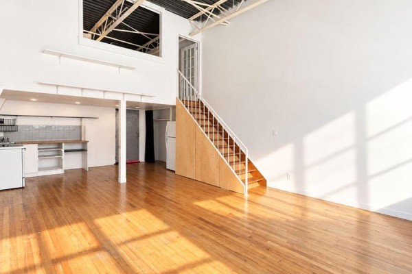 Spacious open-concept living area with high ceilings, hardwood floors, and a kitchen with white cabinets. - 213 - 227 Sterling Road E, Toronto