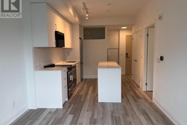 Modern kitchen with white cabinets, stainless steel appliances, and an island, opening to a hallway. - 213 - 3250 Carding Mill Trail, Oakville