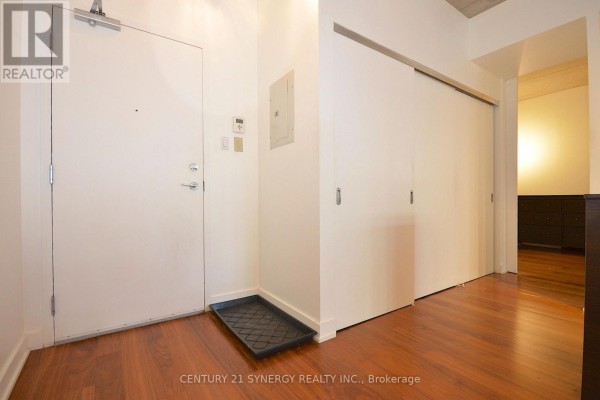 Apartment hallway with a white door, dark wood floor, and sliding closet doors. - 213 - 354 Gladstone Avenue, Ottawa