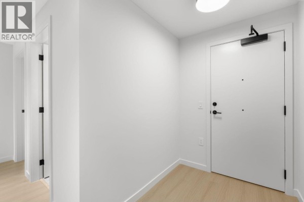 Apartment entrance hallway with a white door and light wood floor. - 213 2015 St. Johns Street, Port Moody