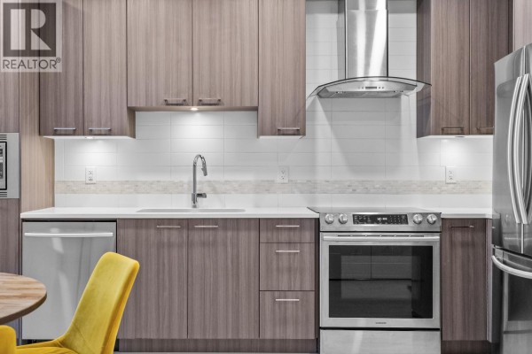Apartment kitchen and dining area with a round table, yellow chairs, and modern cabinetry. - 213 4690 Hawk Lane, Tsawwassen