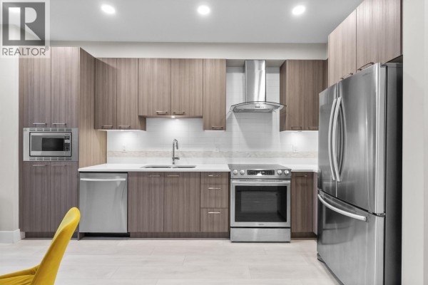 Open concept living and kitchen area with large windows, a sofa, and a dining table. - 213 4690 Hawk Lane, Tsawwassen