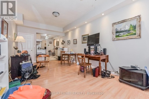 Living area showing multiple seating areas, desks, televisions, and a partial view of the kitchen area. - 213 Main Street E, Minto