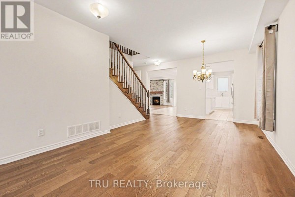Living room with hardwood floors, a staircase, a fireplace visible in the background, and an opening to the kitchen. - 213 Quarter Horse Street, Ottawa
