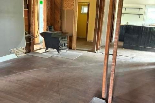 Interior view of an unfinished room with exposed studs, a wood stove, and a doorway to another room. - 213 Second Avenue, Alexander