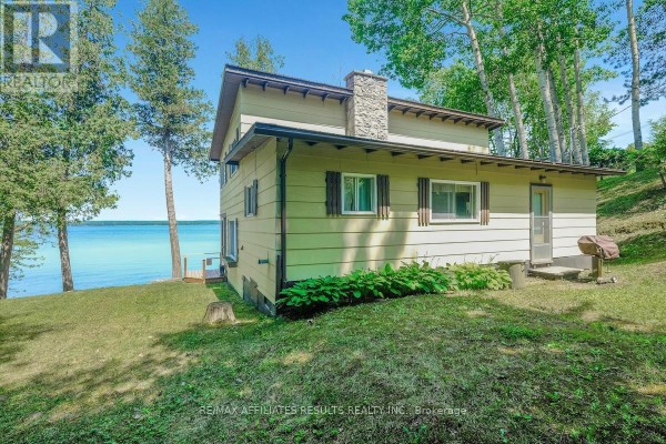 Side exterior of a light yellow house with a stone chimney and a bright blue lake view. - 2130 B River Road, Mcnab/braeside