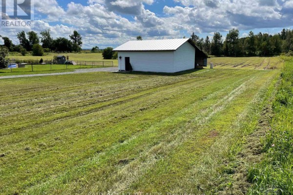 Open grassy area with a white storage building, trees in the background, and a clear sky. - 2130 Du Golf Road, Clarence Rockland