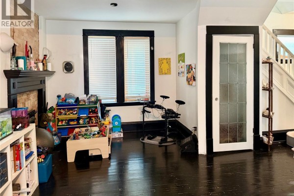 Room with a fireplace, shelves, a window, a door, and children's toys on the dark wood floor. - 2130 Rae Street, Regina