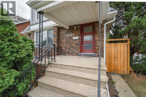 Close-up of the front porch stairs, brickwork, and red front door with frosted glass panels. - 2131 Lincoln Road, Windsor