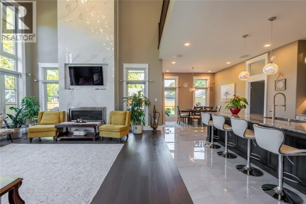 Open concept living and dining area with a large white fireplace, yellow accent chairs, and a kitchen island. - 2132 Huron Shores Drive, Sarnia