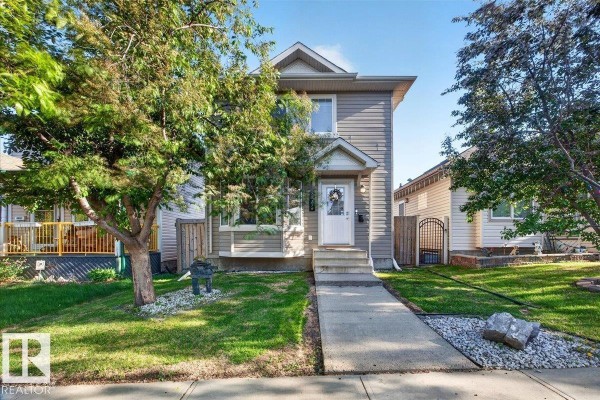 Front view of a two-story house with beige siding, white trim, and mature trees in the yard. - 21339 91 Av Nw, Edmonton