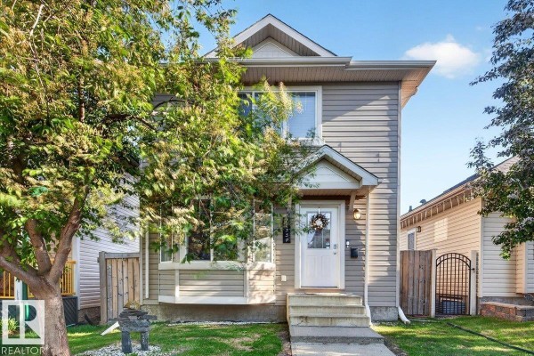 Front facade of a light beige house with a pitched roof, white door, and adjacent fence. - 21339 91 Av Nw, Edmonton