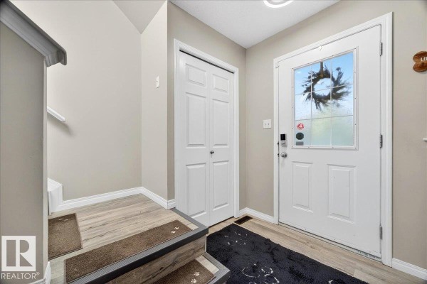 Interior entryway with a white door, closet, stairs leading up, and light wood-look flooring. - 21339 91 Av Nw, Edmonton