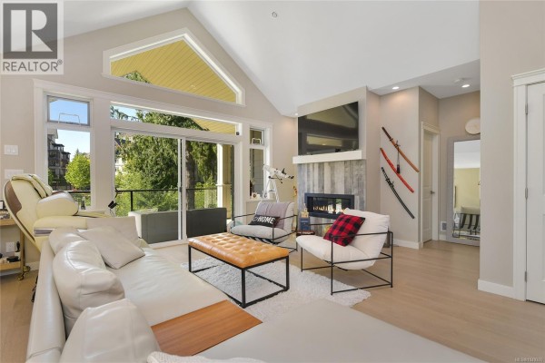 Living room with vaulted ceiling, fireplace, large windows, and a white sectional sofa. - 2136 Champions Way, Langford