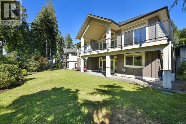 Rear exterior of a house with a large backyard, covered patio, and balcony overlooking the lawn. - 2136 Champions Way, Langford
