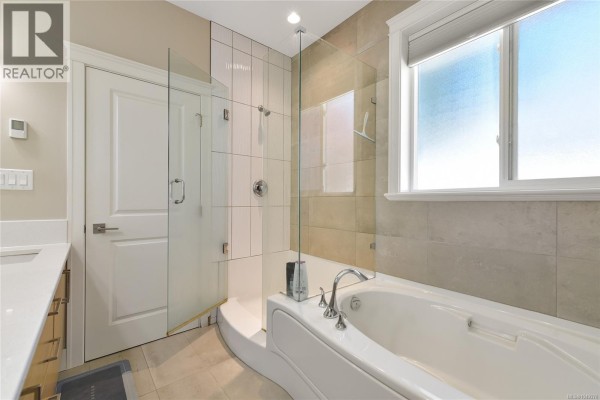 Bathroom with a large soaking tub, glass-enclosed shower, and light beige tile flooring and walls. - 2136 Champions Way, Langford