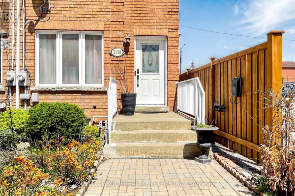 Close-up of the front door and steps of a brick townhouse with a wooden fence. - 2138 Eglinton Avenue W, Toronto