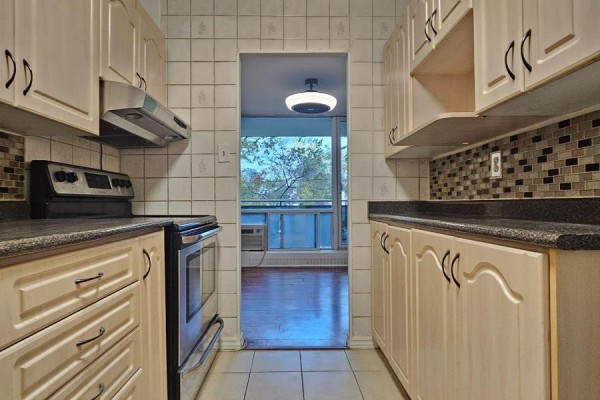 Corner kitchen with white refrigerator, light wood cabinets, mosaic tile backsplash, and dark granite countertops. - 214 - 10 Sunrise Avenue, Toronto