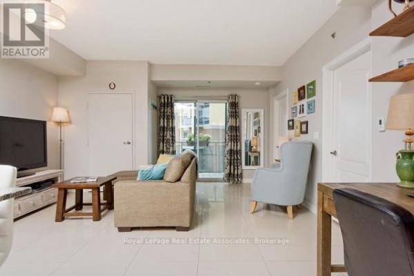 Living room with beige sofa, light blue armchair, wooden coffee table, and sliding glass door to balcony. - 214 - 1421 Costigan Road, Milton