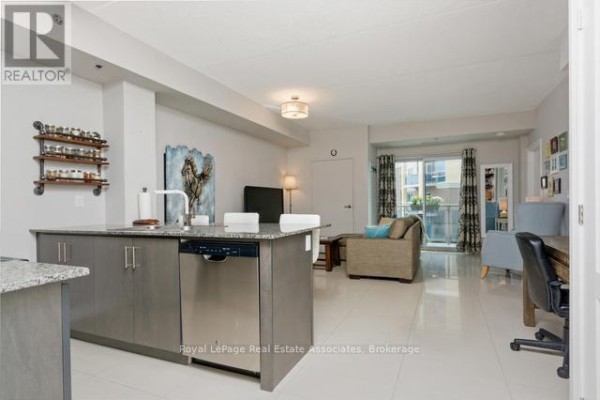 Open concept living space showing kitchen island with dishwasher, living area, and dining table with chairs. - 214 - 1421 Costigan Road, Milton