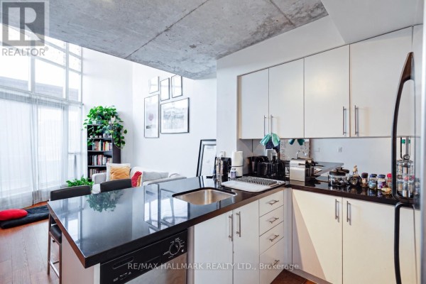 Kitchen island with black granite countertop and sink, facing white cabinets and stainless steel appliances. - 214 - 255 Richmond Street E, Toronto