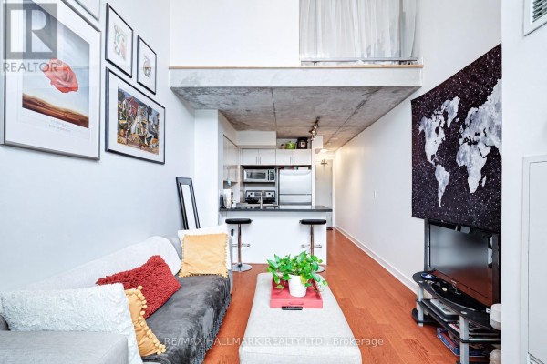 Open concept living area with a sofa, coffee table, and a kitchen island with bar stools. - 214 - 255 Richmond Street E, Toronto