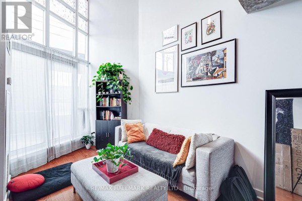Living room with a sofa, ottoman coffee table, bookshelf, and artwork on the wall near a large window. - 214 - 255 Richmond Street E, Toronto