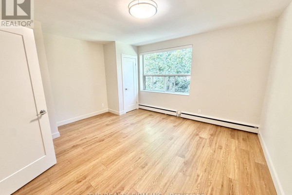 Bedroom with light wood floors, a closet, and a window overlooking trees. - 214 - 55 Beechwood Place, London South