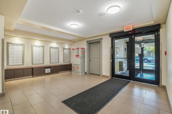 Building lobby with mailboxes, exit sign, and glass doors. - #214 11445 Ellerslie Rd Sw, Edmonton