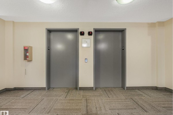Hallway with two grey elevator doors and a fire extinguisher. - #214 11445 Ellerslie Rd Sw, Edmonton