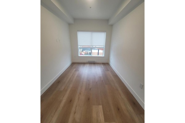 View down a narrow room with light wood floors and a window at the far end. - 214 20282 72b Avenue, Langley