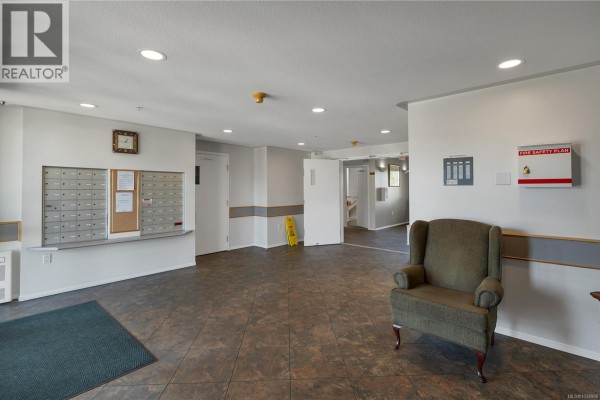 Apartment building lobby with mailboxes, a green armchair, and tiled floors. - 214 280 Dogwood St S, Campbell River