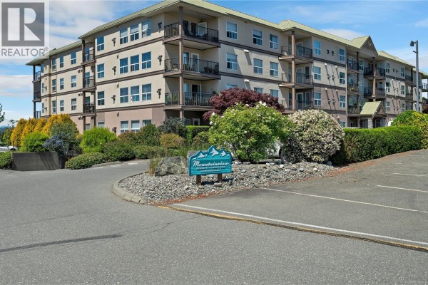 Exterior view of a four-story apartment building with balconies and surrounding landscaping. - 214 280 Dogwood St S, Campbell River