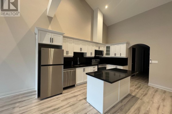 View of the kitchen showing white cabinetry, black countertops, and a central island. - 214 B St Paul Street, St  Catharines