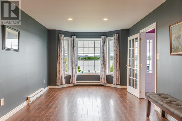 Spacious living room with dark grey walls, wood floors, French doors, and a bay window with a water view. - 214 George Mercer Drive, Bay Roberts