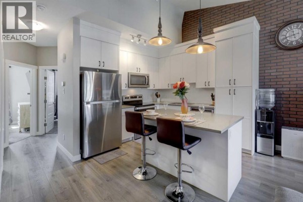 Open concept living and kitchen area with a grey sectional sofa and a brick accent wall. - 214 Livingston Common Ne, Calgary