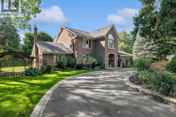 Side view of a brick house with a circular driveway and mature landscaping. - 214 Lovers Lane, Ancaster
