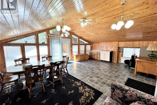 Dining table with six chairs set on a floral rug in a room with wood paneling. - 214 Richard Drive, Barrier Lake