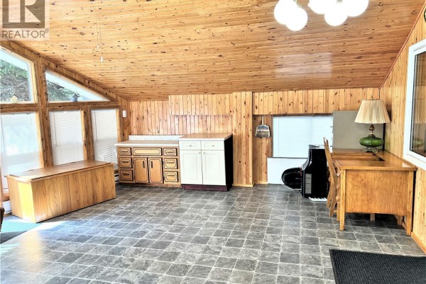 Living area with a floral couch and dining table near double glass doors, featuring wood paneling. - 214 Richard Drive, Barrier Lake