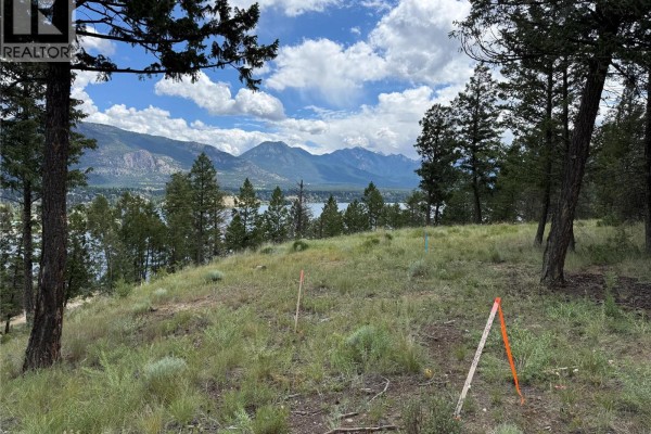 A picnic table and four Adirondack chairs sit in a grassy area surrounded by trees. - 2140 22nd Street, Invermere