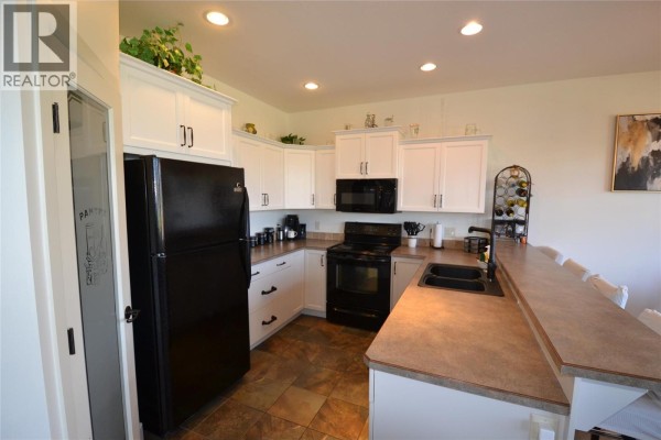 Living room with a fireplace, large television, leather sofas, and a glass coffee table. - 2148 Serrento Lane, West Kelowna
