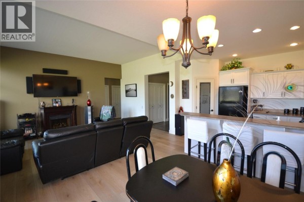 Open concept living and dining area with leather furniture, a view into the kitchen, and light wood flooring. - 2148 Serrento Lane, West Kelowna