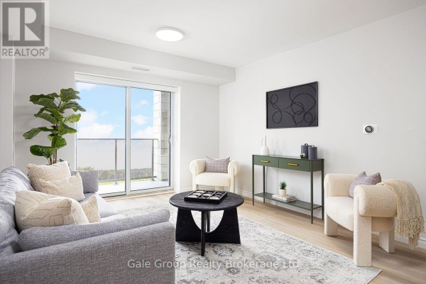 Living room featuring a grey sofa, patterned rug, and a large window overlooking the city. - 215 - 425 Watson Parkway N, Guelph