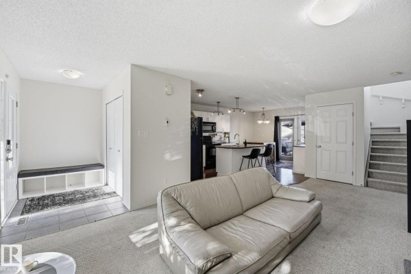 Living room with a beige couch, open concept to the kitchen with black appliances and island. - 215 85 St Sw, Edmonton