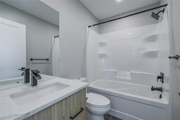 Bathroom with white bathtub, toilet, vanity with quartz countertop, and black fixtures. - 215 Devon Avenue, Winnipeg