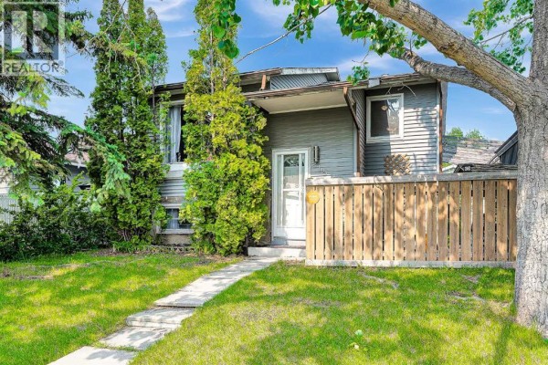 Side view of the front exterior showing grey siding, a white door, and a wooden fence. - 215 Erin Woods Drive Se, Calgary