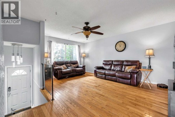 Living room with hardwood floors, two brown leather sofas, a ceiling fan, and a large wall clock. - 215 Erin Woods Drive Se, Calgary